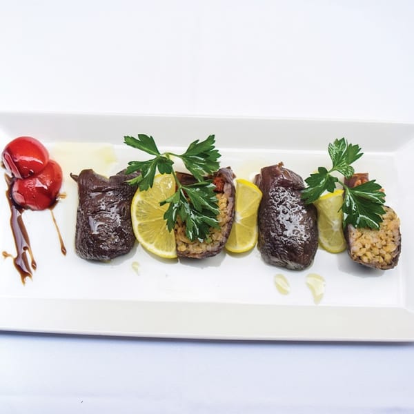Turkish stuffed eggplant with rice, lemon, parsley, and red peppers on a white plate.