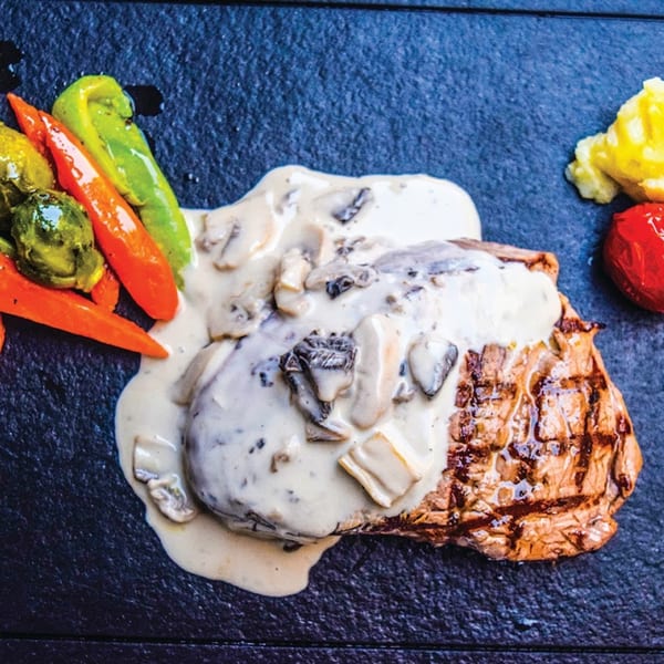 Grilled steak with creamy mushroom sauce, roasted carrots, green peppers, and brussels sprouts.