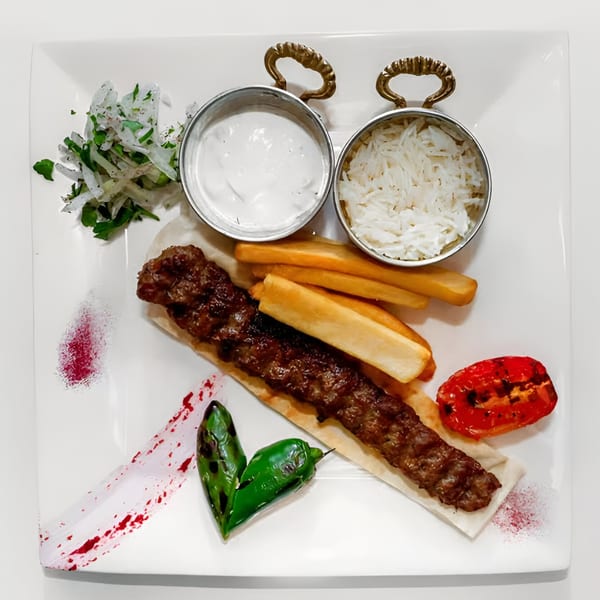 Turkish Adana kebab with rice, yogurt, grilled tomato, peppers, and onions on a white plate.
