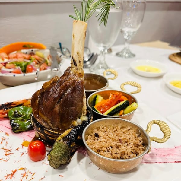 A Turkish lamb shank with rosemary, grilled vegetables, rice, and a side salad.