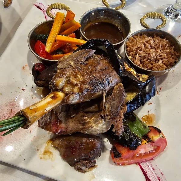 Turkish lamb shank with roasted vegetables, rice, and gravy served on a white plate.