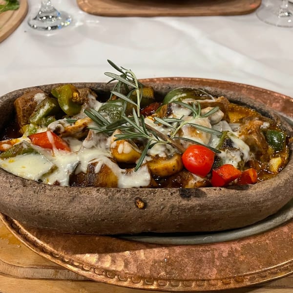 A Turkish clay pot dish with melted cheese, green peppers, cherry tomatoes, and rosemary.
