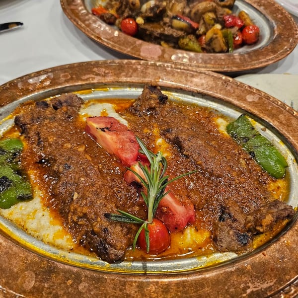 Turkish kebab with sauce, tomatoes, green peppers, and rosemary on a copper plate.